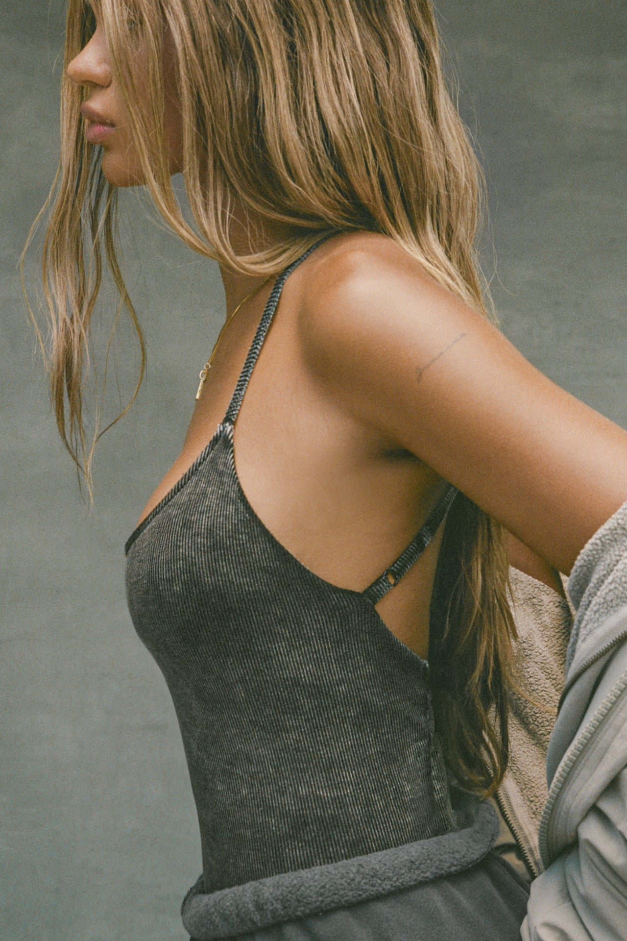 Side view of model posing in the fitted charcoal washed rib Cross Back Cami with a scoop neckline and thin adjustable straps that criss cross in the back