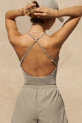 Back view of model posing in the fitted dune washed rib Cross Back Cami with a scoop neckline and thin adjustable straps that criss cross in the back