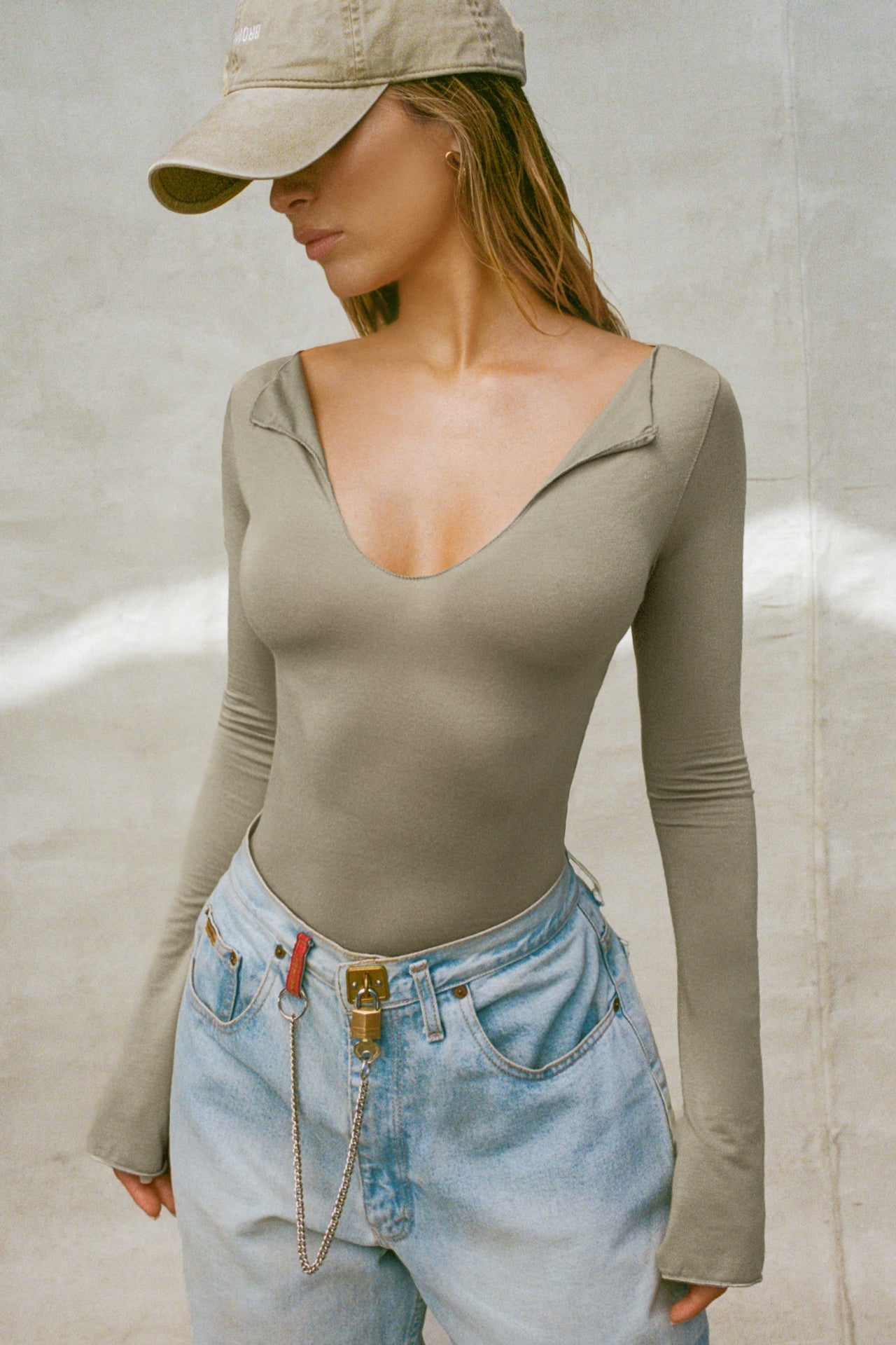 Front view of model posing in the fitted sage modal Notched V Neck Long Sleeve top with a deep notched V-neckline, extra long sleeves and small side slits at the hem