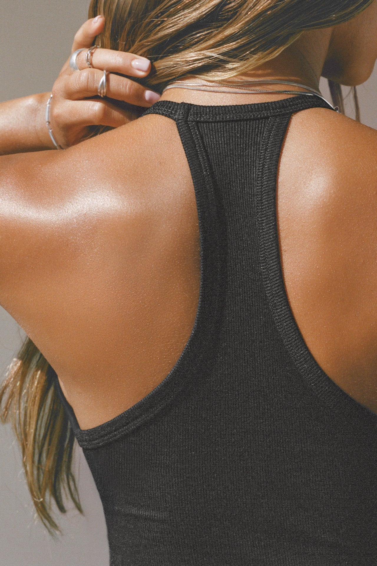 Back detail view of model posing in the fitted black flexrib Plunge Racerback Tank top with a racerback silhouette.