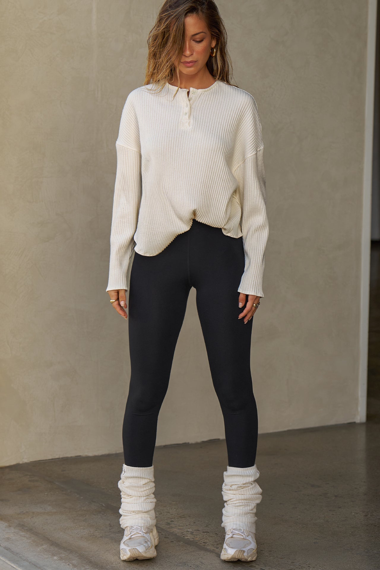 Full body front view of model posing in the relaxed-fit natural luxe knit Henley Pullover long sleeve top with a buttoned henley neckline and curved hem.