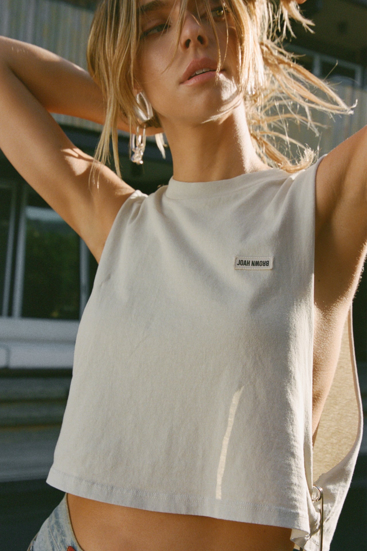 Front view of model posing in the relaxed fit fog cotton Cut Off Boyfriend Tank with low cut armholes, a crew neckline and a joah brown logo patch at the upper left chest