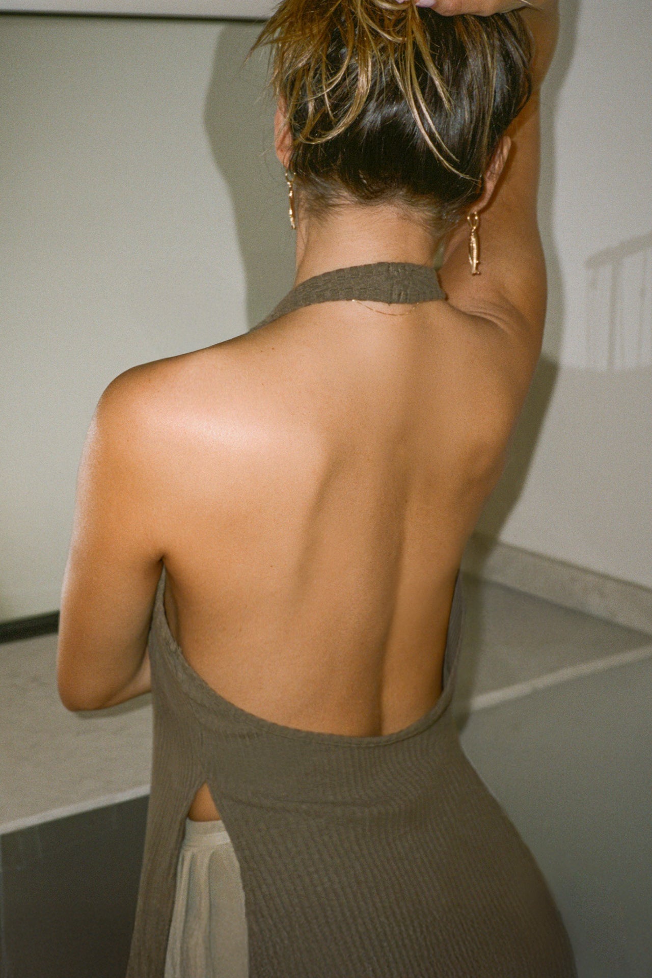 Back view of model posing in the army luxe knit Split Front Halter Tank with an open back and side slits
